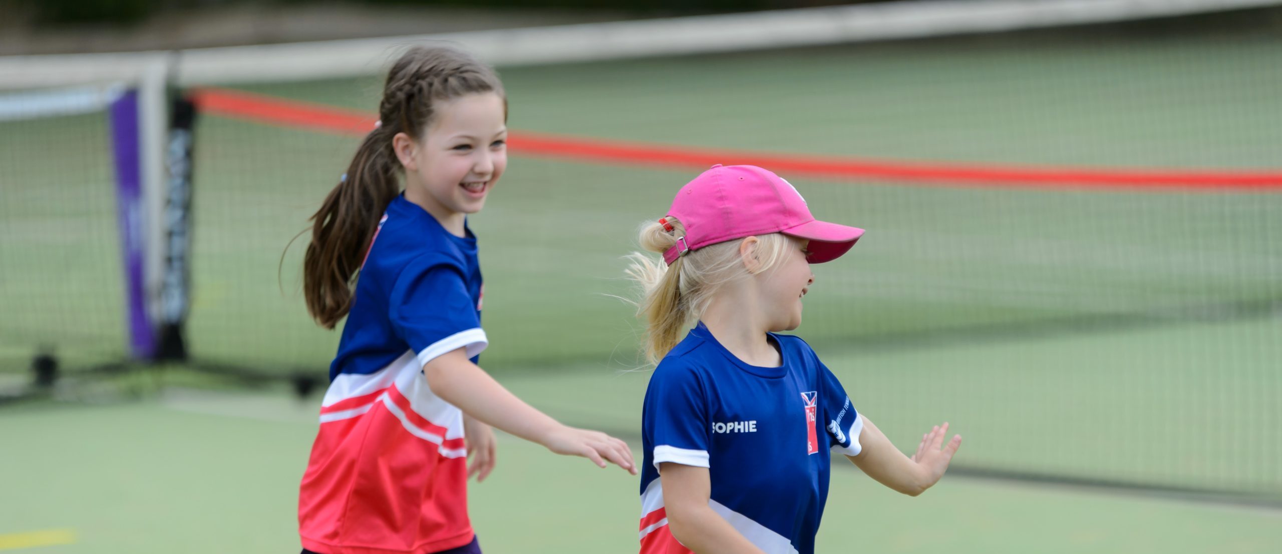 Two primary school girls running on a tennis court