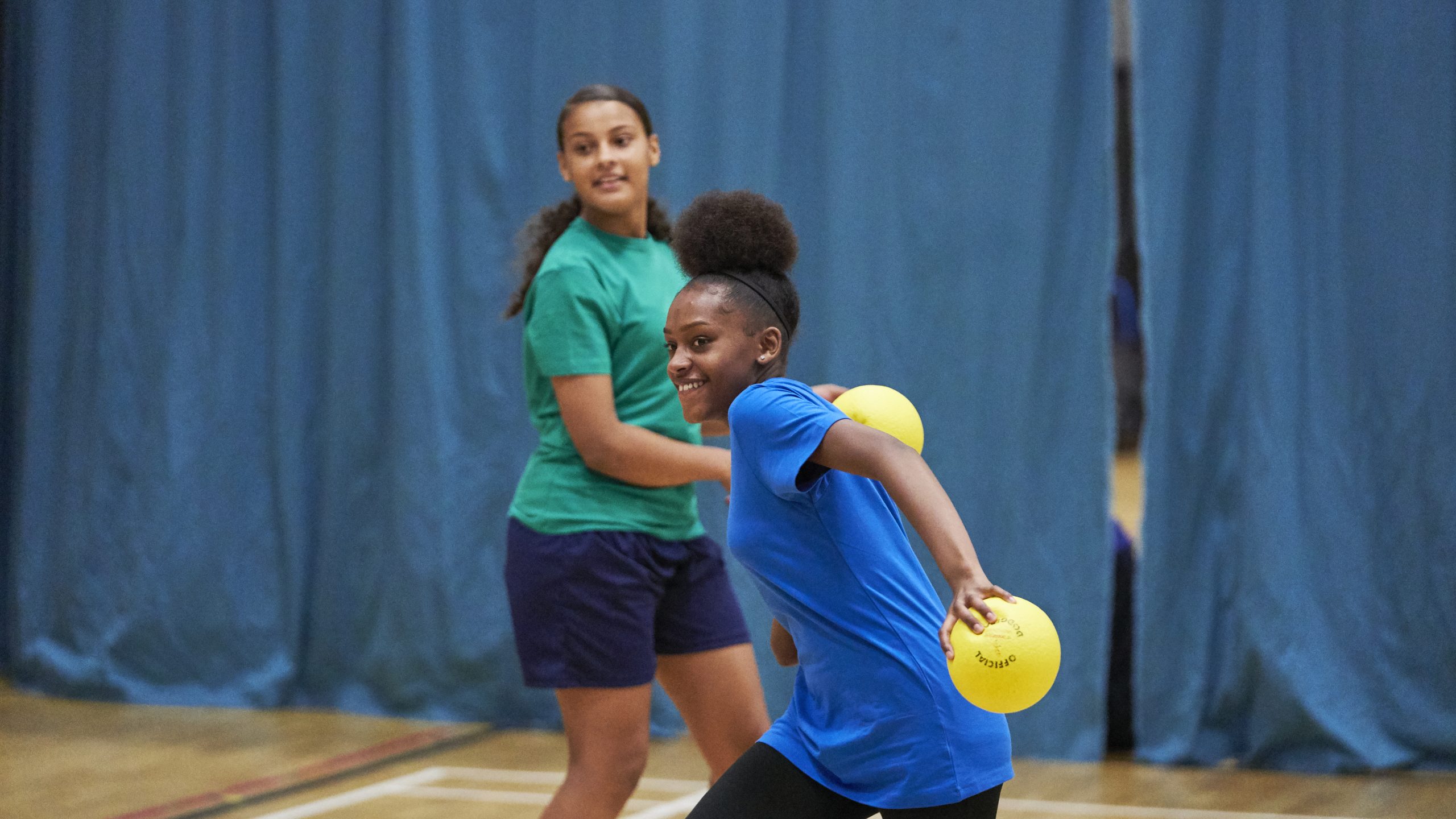 A black teenage girl and a mixed race teenage girl playing dodgeball