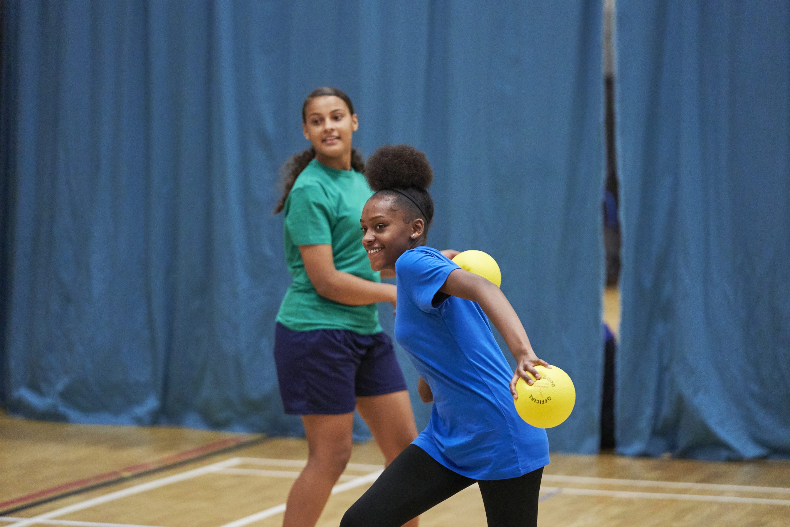 A black teenage girl and a mixed race teenage girl playing dodgeball