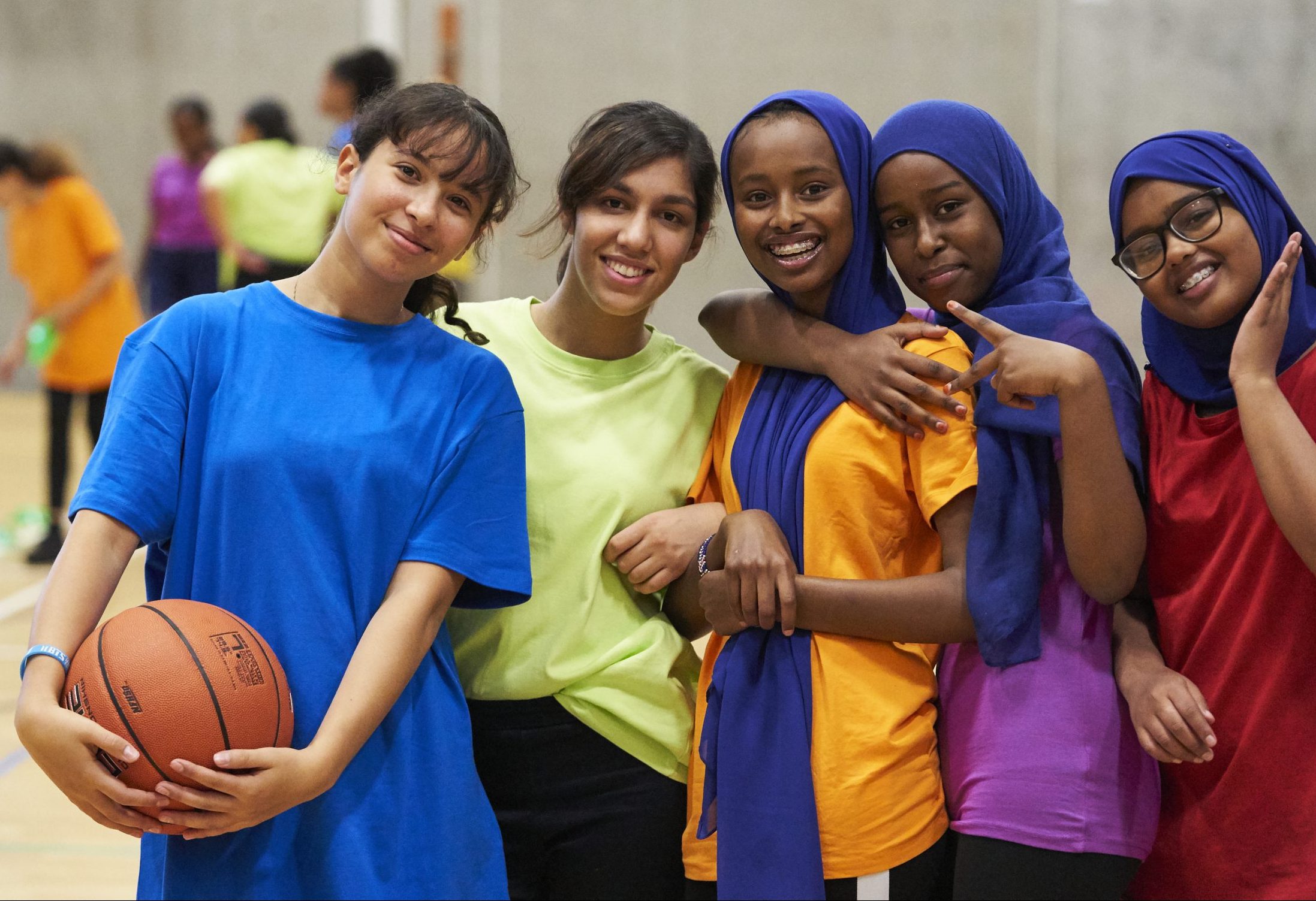 A group of school girls smiling together on a basketball court
