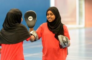 Two teenage girls wearing headscarves boxing