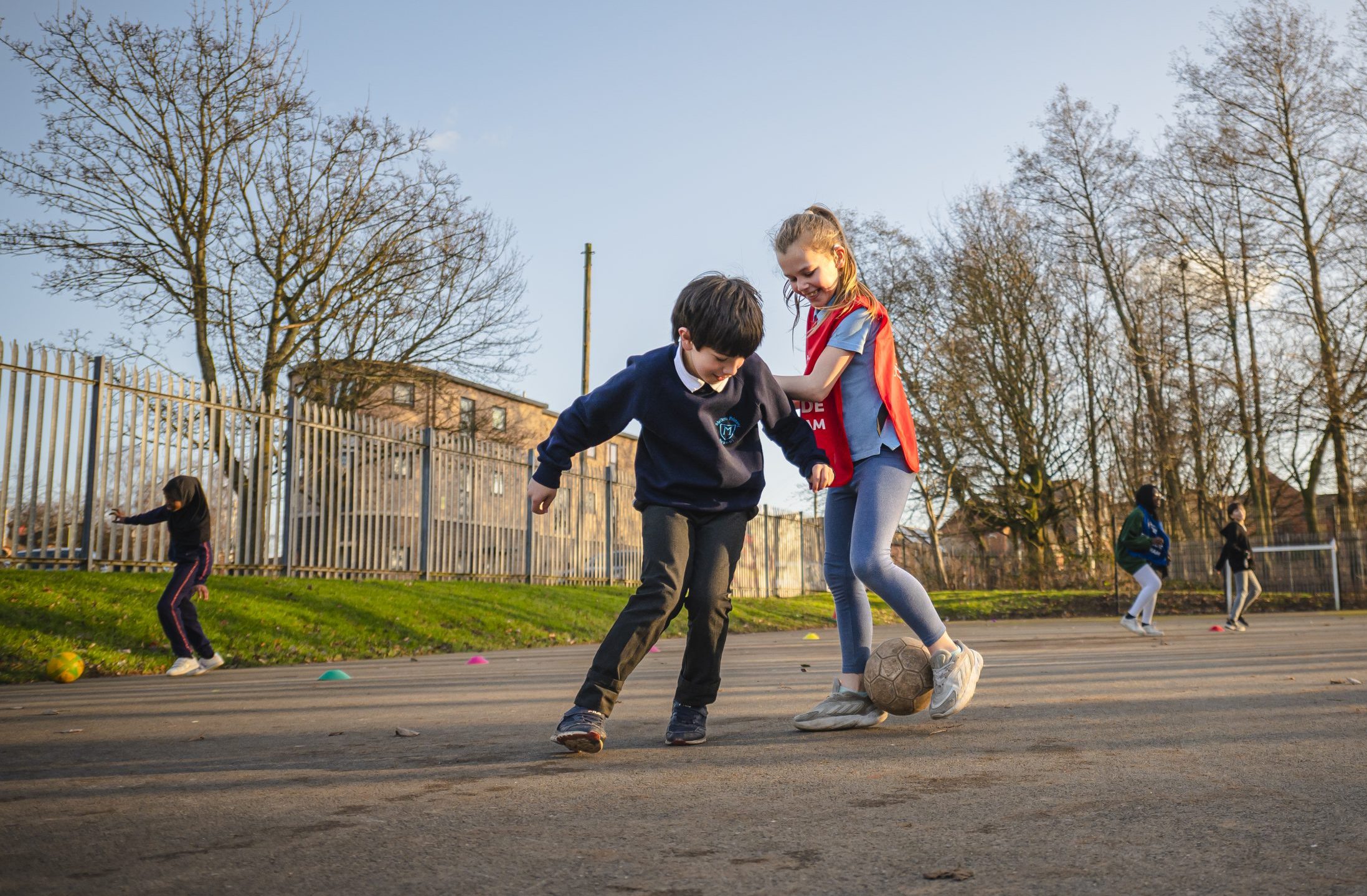 A young boy and girl playing football together at school
