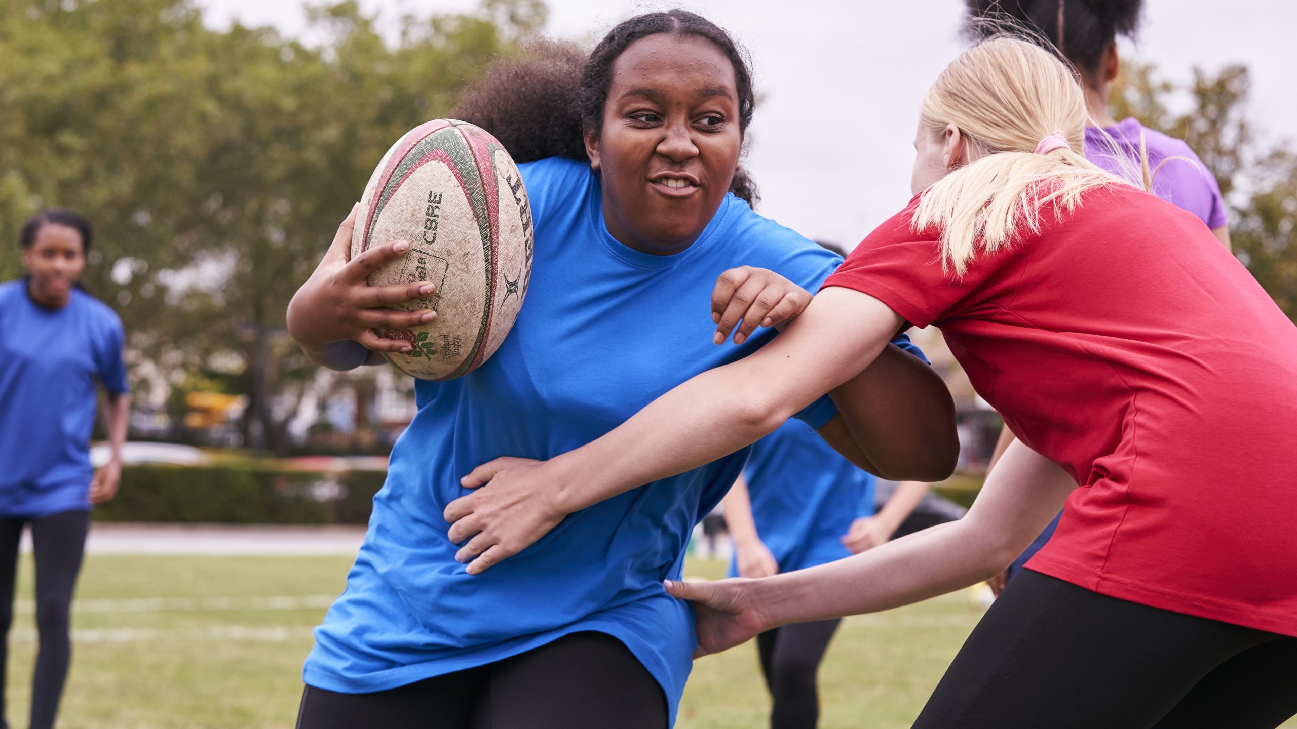 A white teenage girl rugby tackling a black teenage girl