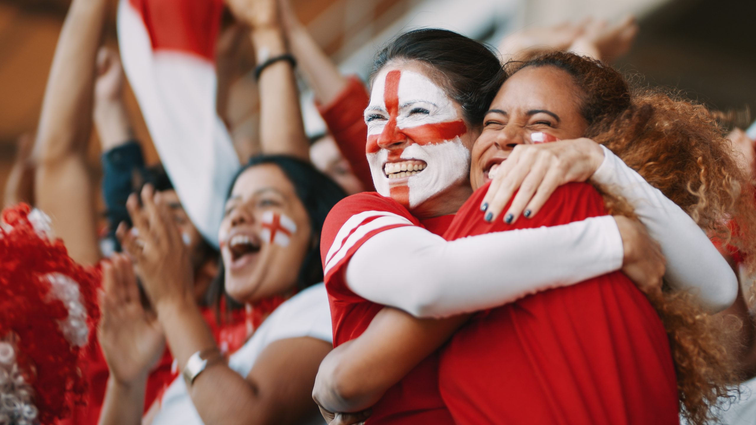 Two female football fans celebrating a goal. One has the England flag painted on her face