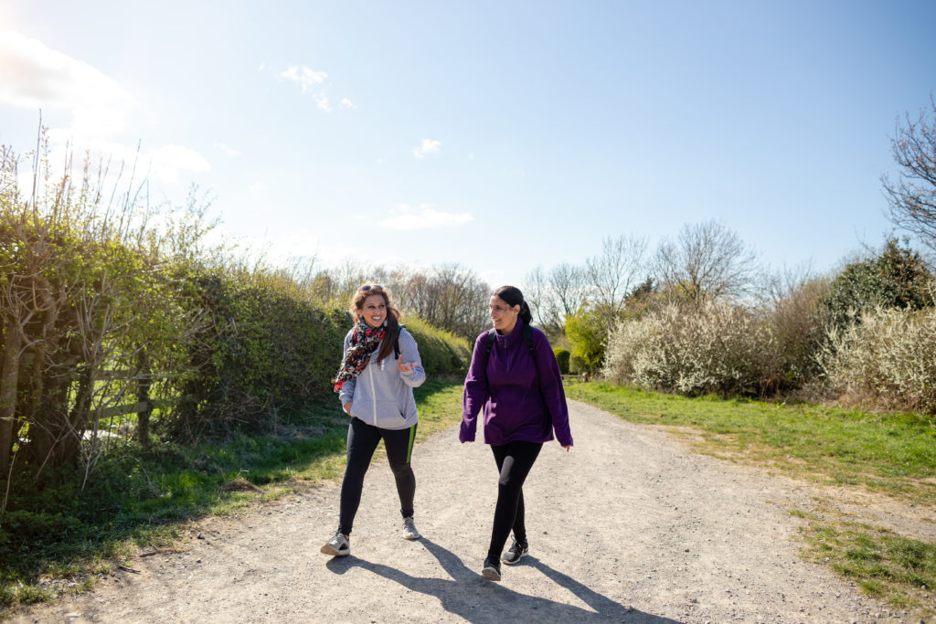 two women walk together on a gravel path in the sunshine