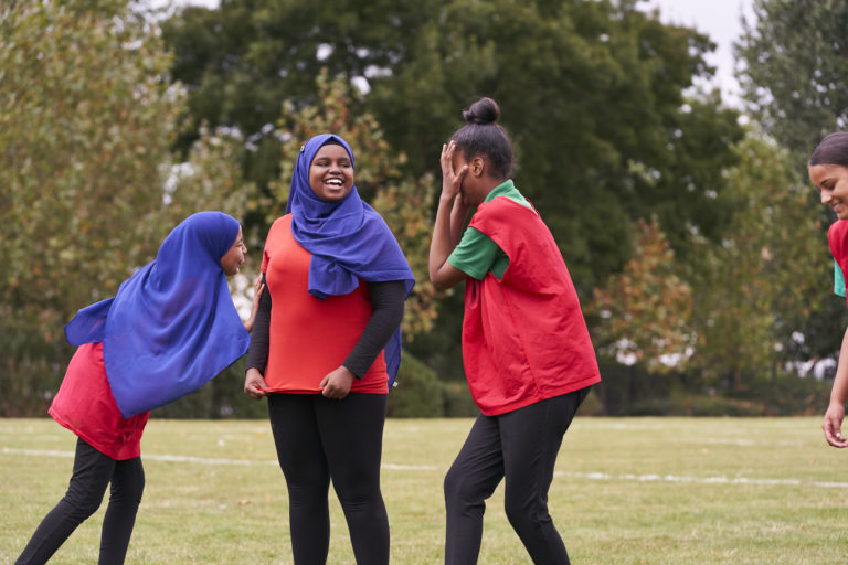 Two muslim teenagers wearing headscarfs and a black teenager plauing team sport