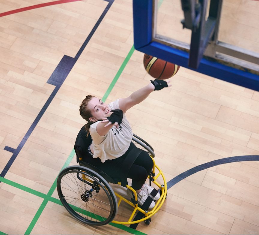 White woman in a wheelchair throwing a basketball