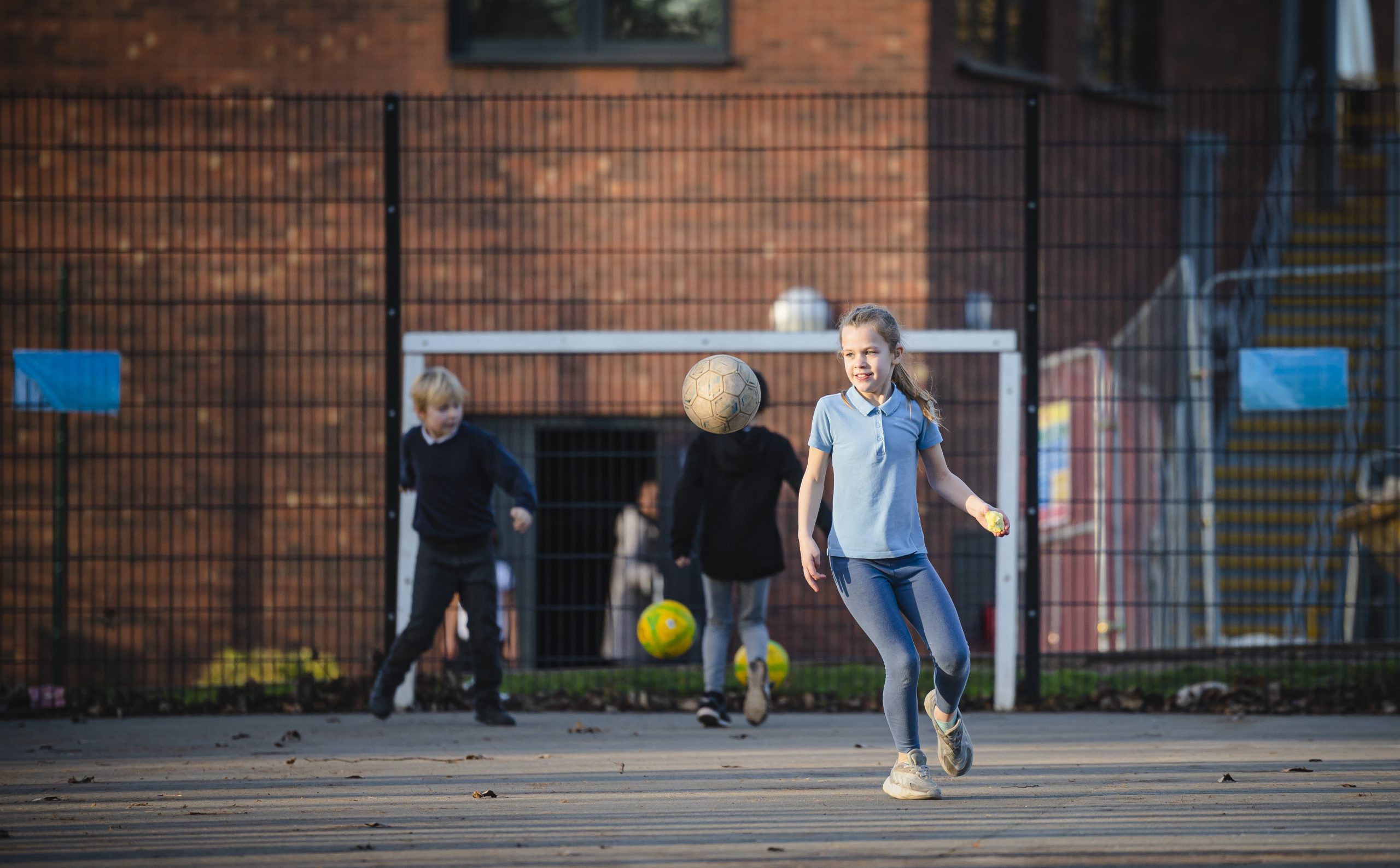 Young blonde girl playing football at school