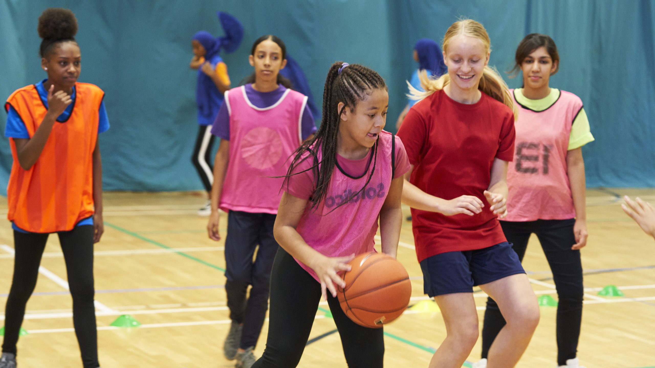 Teenage girls playing basketball. The girl with the ball is mixed raced and wears her hair in braids
