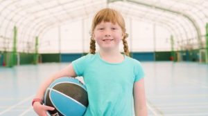 A young girl with braided red hair holding a basketball