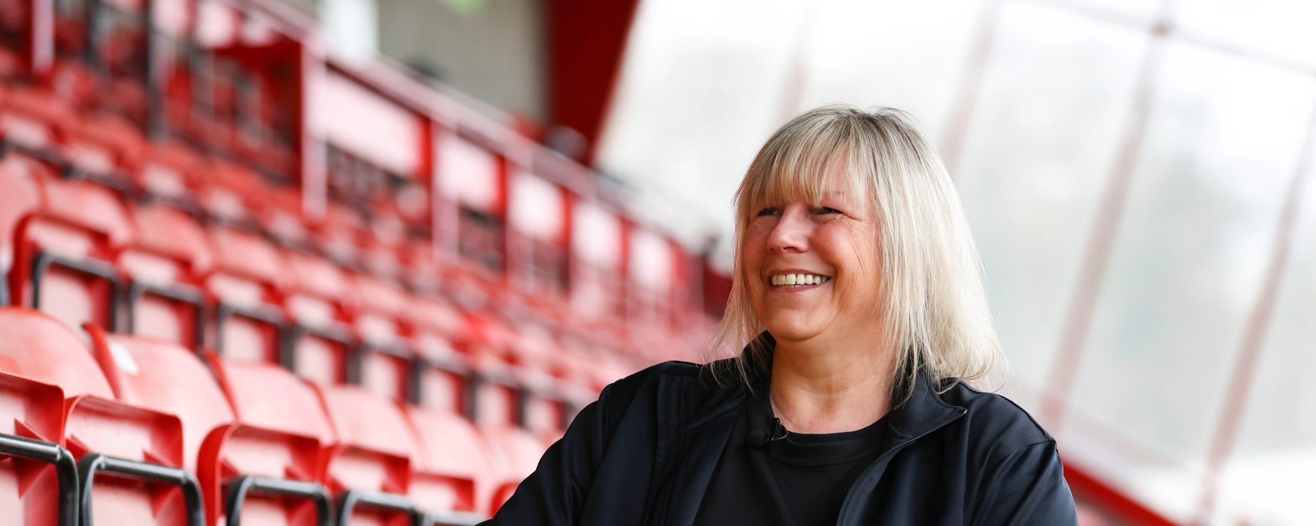 A white woman aged 50-55 sat in football stands smiling