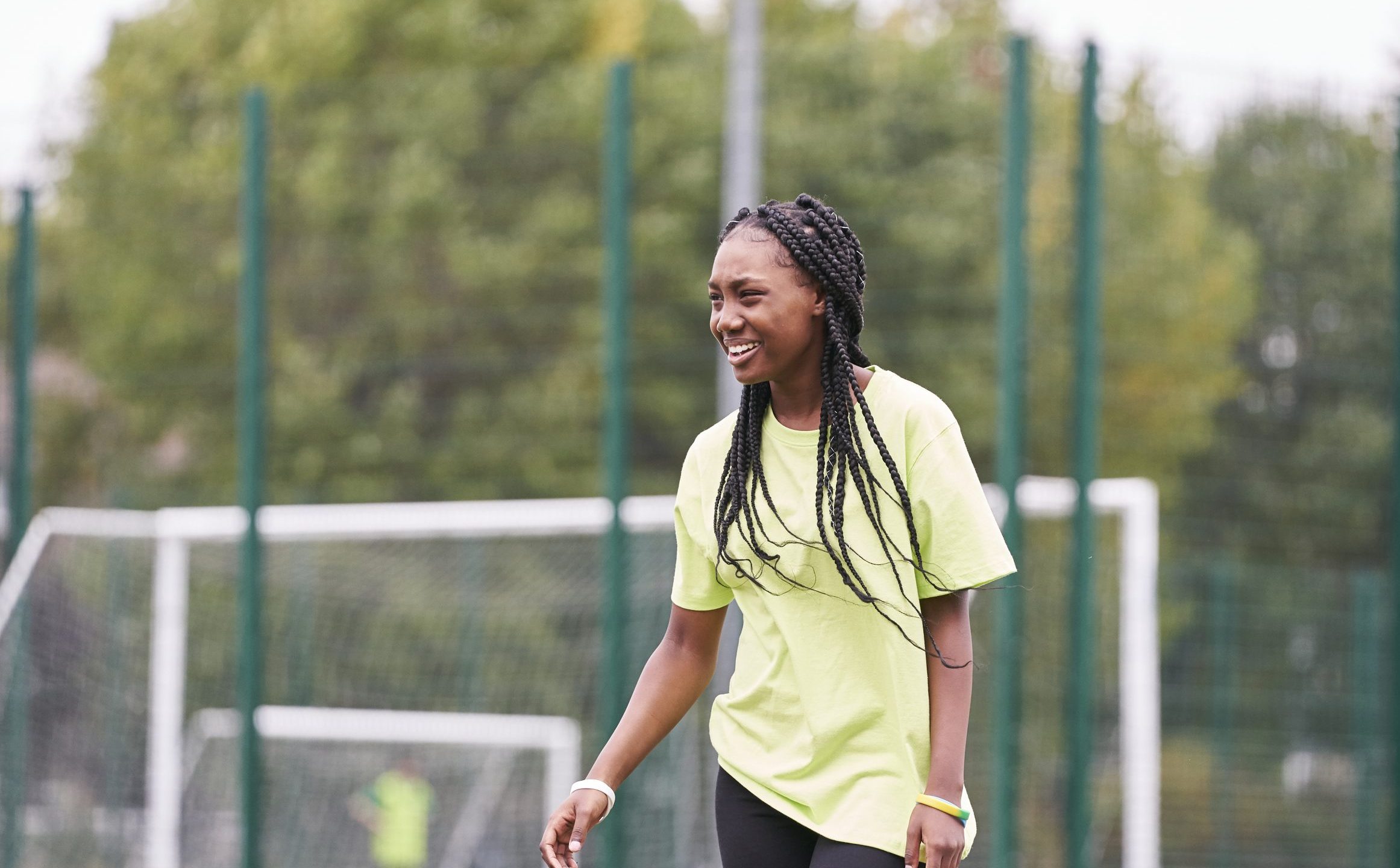 A young black teenager with braided hair laughing while playing football