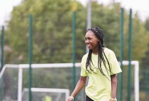 A young black teenager with braided hair laughing while playing football