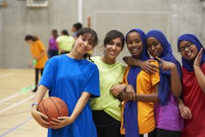 A group of girls playing basketball, three girls are wearing hijabs