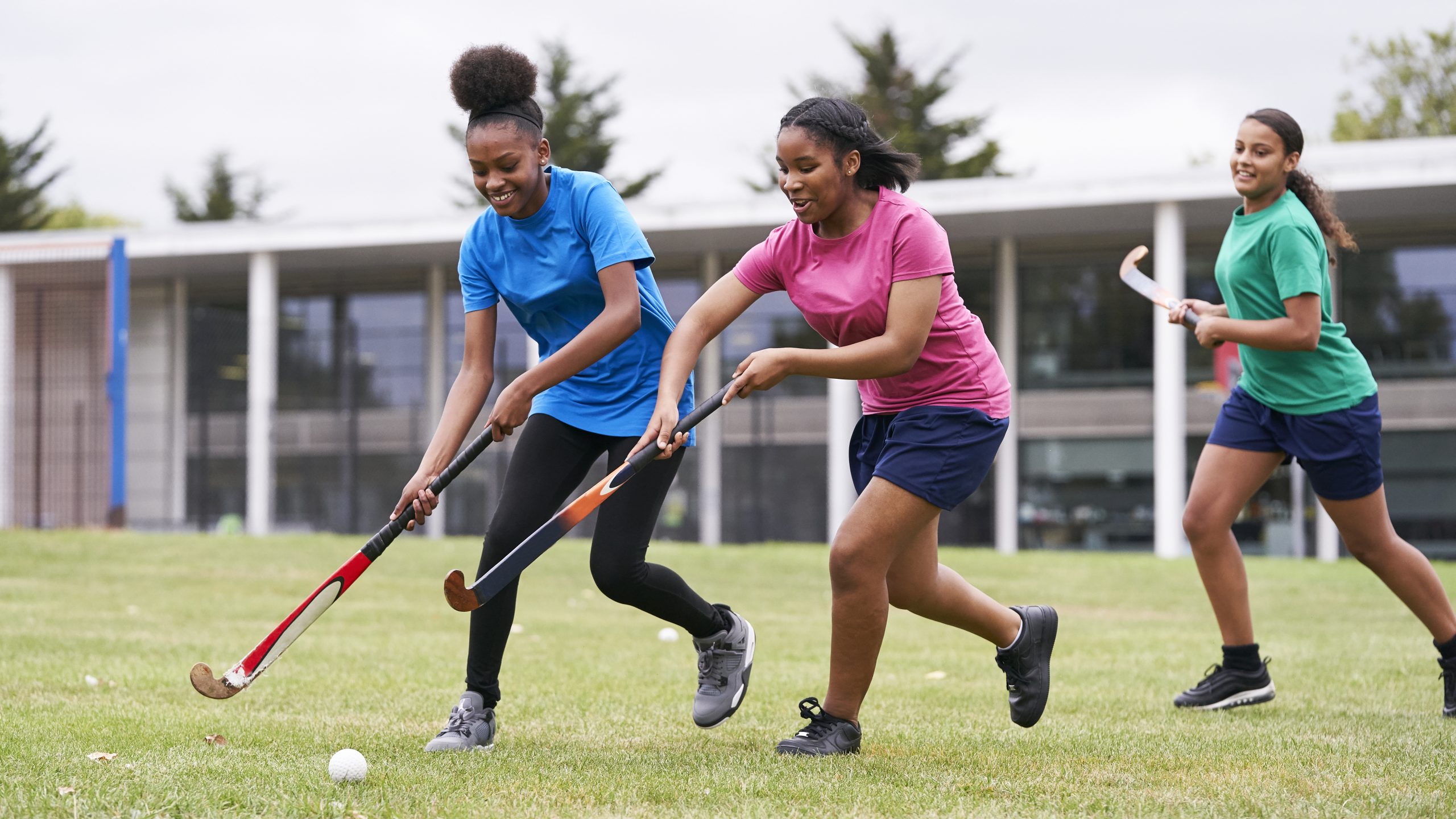 Two black teenage school girls playing hockey on grass
