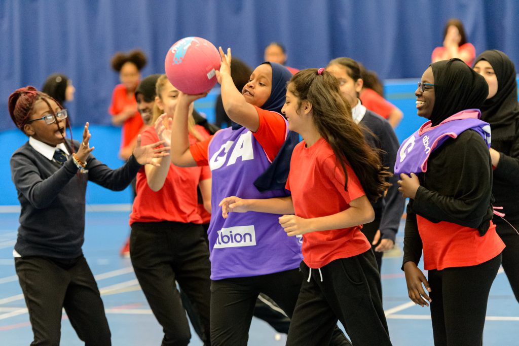 Group of teenage school girls playing netball. GA wearing a hijab has the ball. 