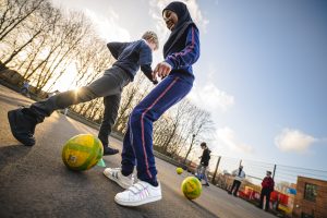 A young Muslim girl and a young white boy playing football together at school