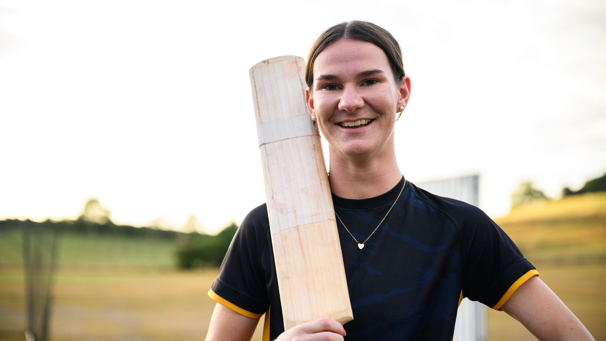 A white teenage girl with a cricket bat, smiling